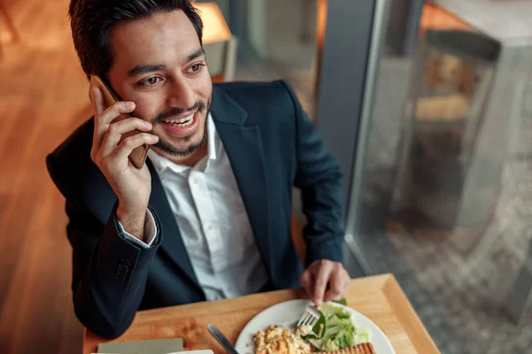 Indian businessman is talking phone with client during lunch time in cozy cafe. High quality photo