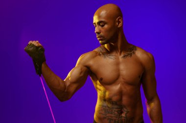 Man performs exercises with expander on studio background with color filter. Strength and motivation