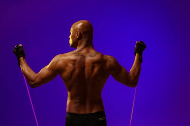Man performs exercises with expander on studio background with color filter. Strength and motivation