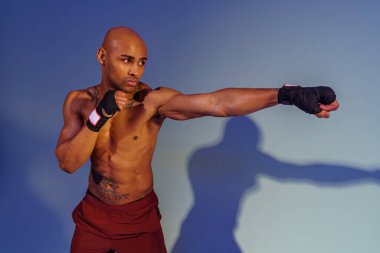 Professional kickboxer is training and practicing punch on studio background with color filter