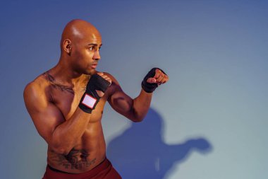 Professional kickboxer is training and practicing punch on studio background with color filter