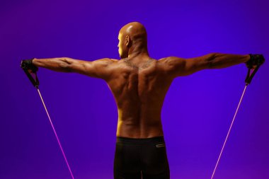 Man performs exercises with expander on studio background with color filter. Strength and motivation