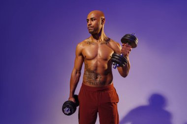 Muscular man doing exercise with weight dumbbells on studio background with color filter