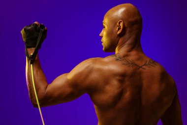 Man performs exercises with expander on studio background with color filter. Strength and motivation