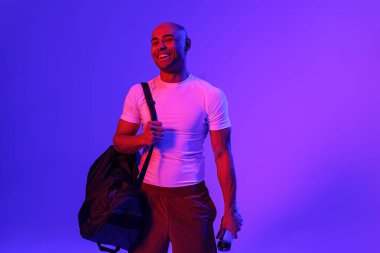 Sporcu elinde su şişesi ve çanta ile stüdyonun arka planına bakarak menekşe filtresi kullanıyor.