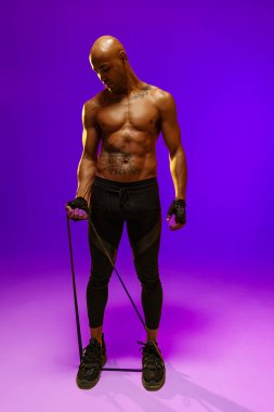 Man performs exercises using resistance band on studio background. Strength and motivation