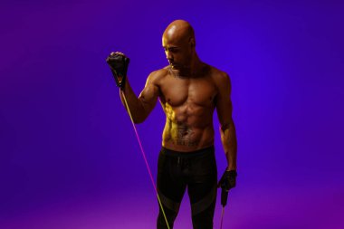 Man performs exercises with expander on studio background with color filter. Strength and motivation