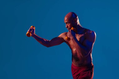 Muscular man doing exercise with weight dumbbells on studio background with color filter