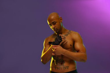 Muscular man puts on fighting gloves posing on studio background with color filter