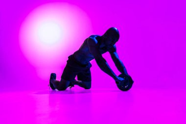 Muscular man working on his abs with a ab roller on studio background with color filter