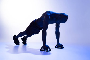 Atletik adam, stüdyo arka planında renk filtresi kullanarak şınav çekiyor.