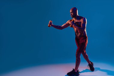 Muscular man doing exercise with weight dumbbells on studio background with color filter
