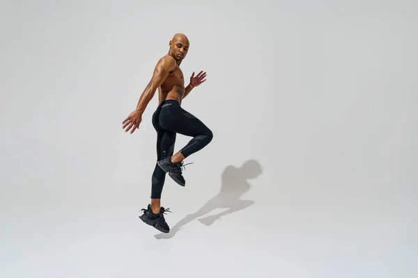 Active sporty man with naked torso jumping on white studio background. Dynamic movement
