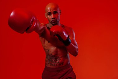 Man wearing boxing gloves practicing for fight on studio background with color filter