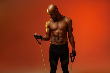 Man performs exercises with expander on studio background with color filter. Strength and motivation