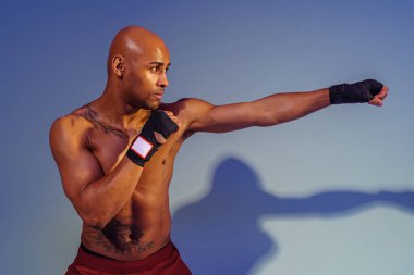 Professional kickboxer is training and practicing punch on studio background with color filter
