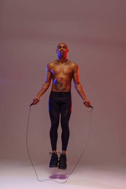 Stüdyo arka planında renk filtresiyle ip atlayan bir adam. En iyi kardiyo çalışması