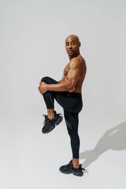 Man with naked torso doing leg stretching exercises before workout on white studio background