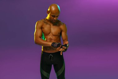 Muscular man puts on fighting gloves posing on studio background with color filter