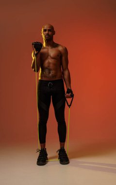 Man performs exercises with expander on studio background with color filter. Strength and motivation