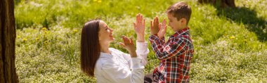 Mutlu anne küçük oğluyla oynuyor, parkta çimenlerde otururken el çırpıyor. Oyun oyna.