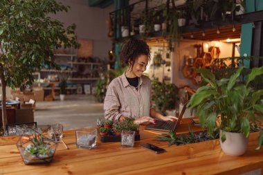 Florist woman works in her small floral business surf for information about plants using laptop