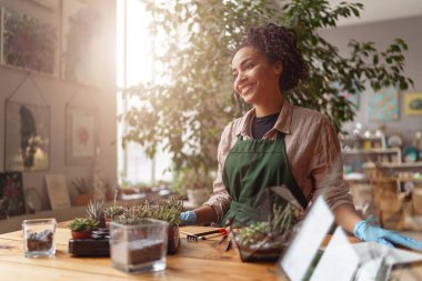 Young woman florist wearing apron taking care of plant in floral studio. High quality photo