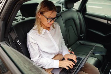 Dizüstü bilgisayarda çalışan kadın muhasebeci ofise giderken arabanın arka koltuğunda oturuyor. Yüksek kalite fotoğraf