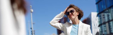 Women in trendy outfits walk outside near business center. Blurred background