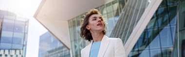 Attractive woman in trendy outfit standing on skyscrapers cityscape background and enjoy sun