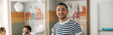 Smiling businessman in casual clothes standing in modern office on colleagues background