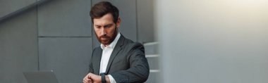 Businessman in suit working laptop and looking on wriste watch near office. Business concept