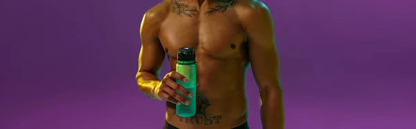 スポーティ男とともにMuscled裸胴保持ボトルとともに水でスタジオ背景にカラーフィルター — ストック写真
