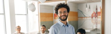 Smiling businessman standing in modern office on colleagues background