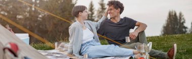 Happy boyfriend and girlfriend laughing and relaxing at wild nature at tent. Romantic rural weekend.