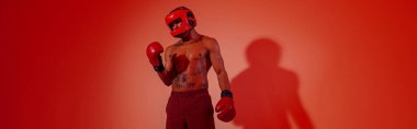 Man wearing head guard and boxing gloves practicing for fight on studio background with color filter
