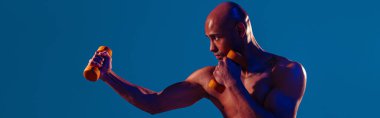 Muscular man doing exercise with weight dumbbells on studio background with color filter