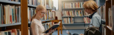 Friends student sit on floor near bookshelves in library and studying. Education concept