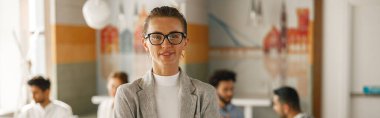Smiling businesswoman in suit standing in modern office on colleagues background