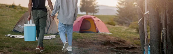 stock image Rear on couple walking at camping place hand in hand and carrying portative fridge. Vacation outdoor