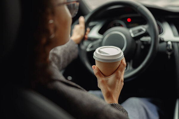Close up of young woman drinking take out coffee when driving to work in car. High quality photo