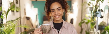 Woman floristic studio owner standing with cup of tea and laptop during break. High quality photo