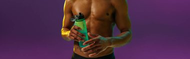 Sporty man with muscled naked torso holding bottle with water on studio background with color filter