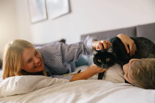 주말에 집에서 침대에 고양이를 쓰다듬고 어머니 와아들의 — 스톡 사진