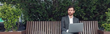 Male businessman working on laptop at lunchtime sitting on bench near office. Blurred background