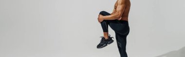 Man with naked torso doing leg stretching exercises before workout on white studio background