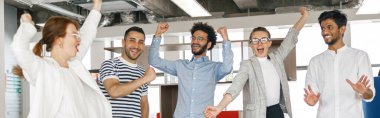 Happy group of businesspeople laughing cheerfully and raised their hands up in a modern workplace