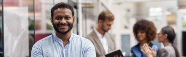 Handsome african businessman standing in modern office on colleagues background and looking camera