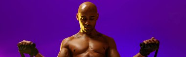 Man performs exercises with expander on studio background with color filter. Strength and motivation