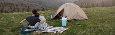 Rear on couple hugging and resting in mountains. On peak of mount, Beautiful view. Together. Rear.